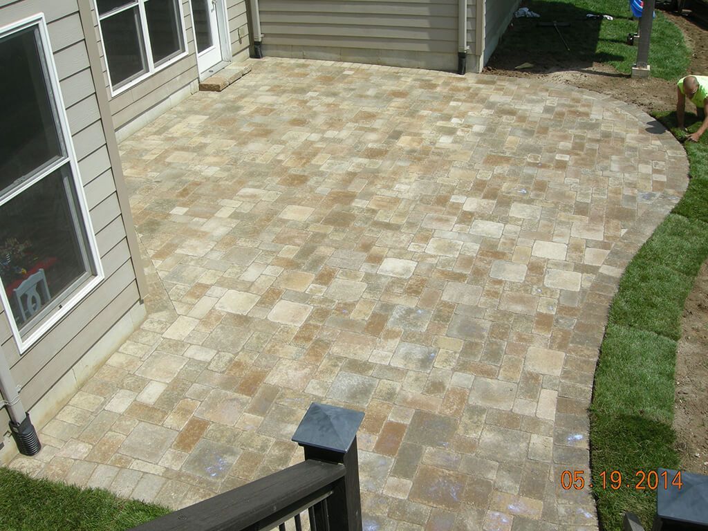 Brick patio with curving edge, next to green lawn, house with windows.