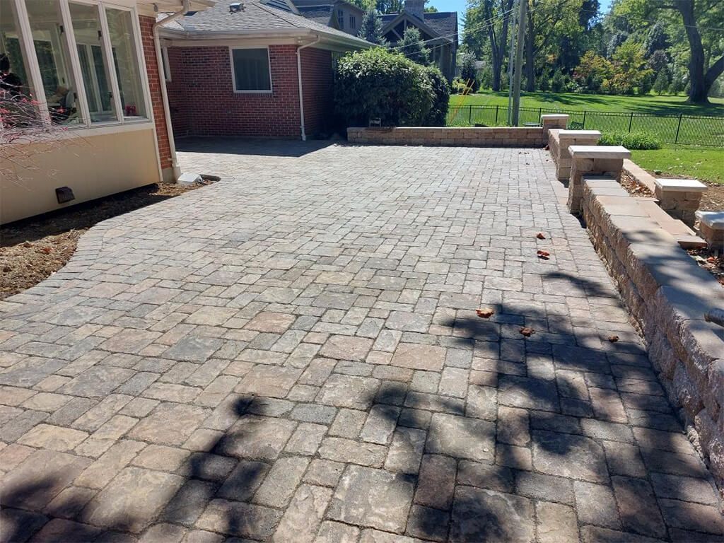 Brick paver patio with retaining wall, next to a red brick building, on a sunny day.