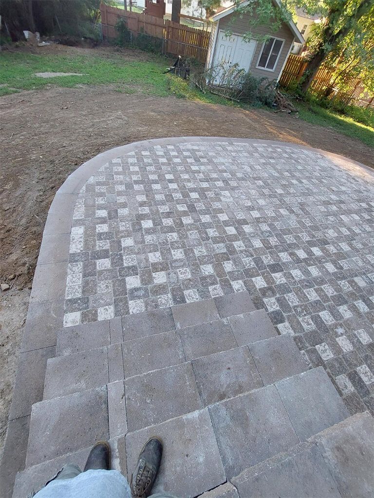 Stone patio with steps, gray pavers, green yard, and a shed.