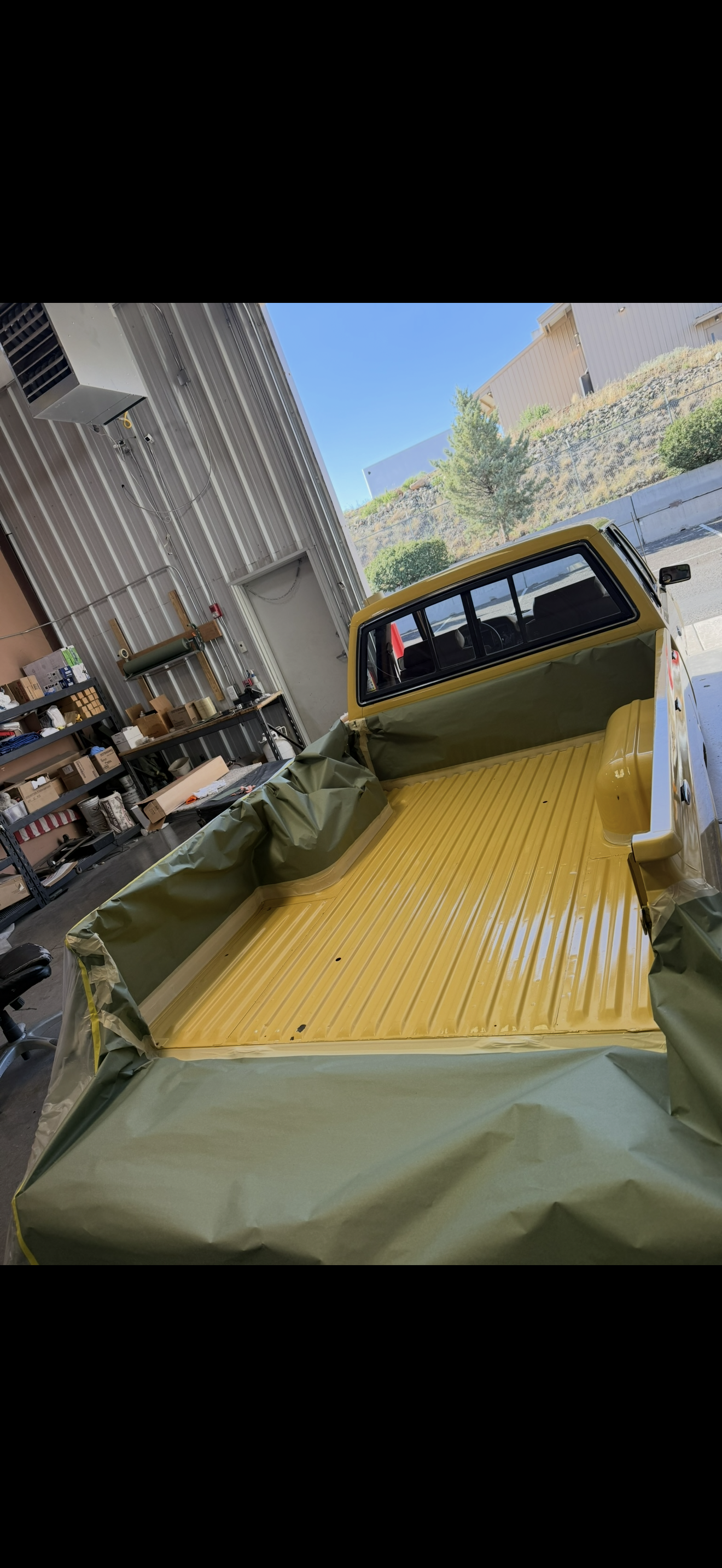 A yellow pickup truck bed with a green liner, outdoors.