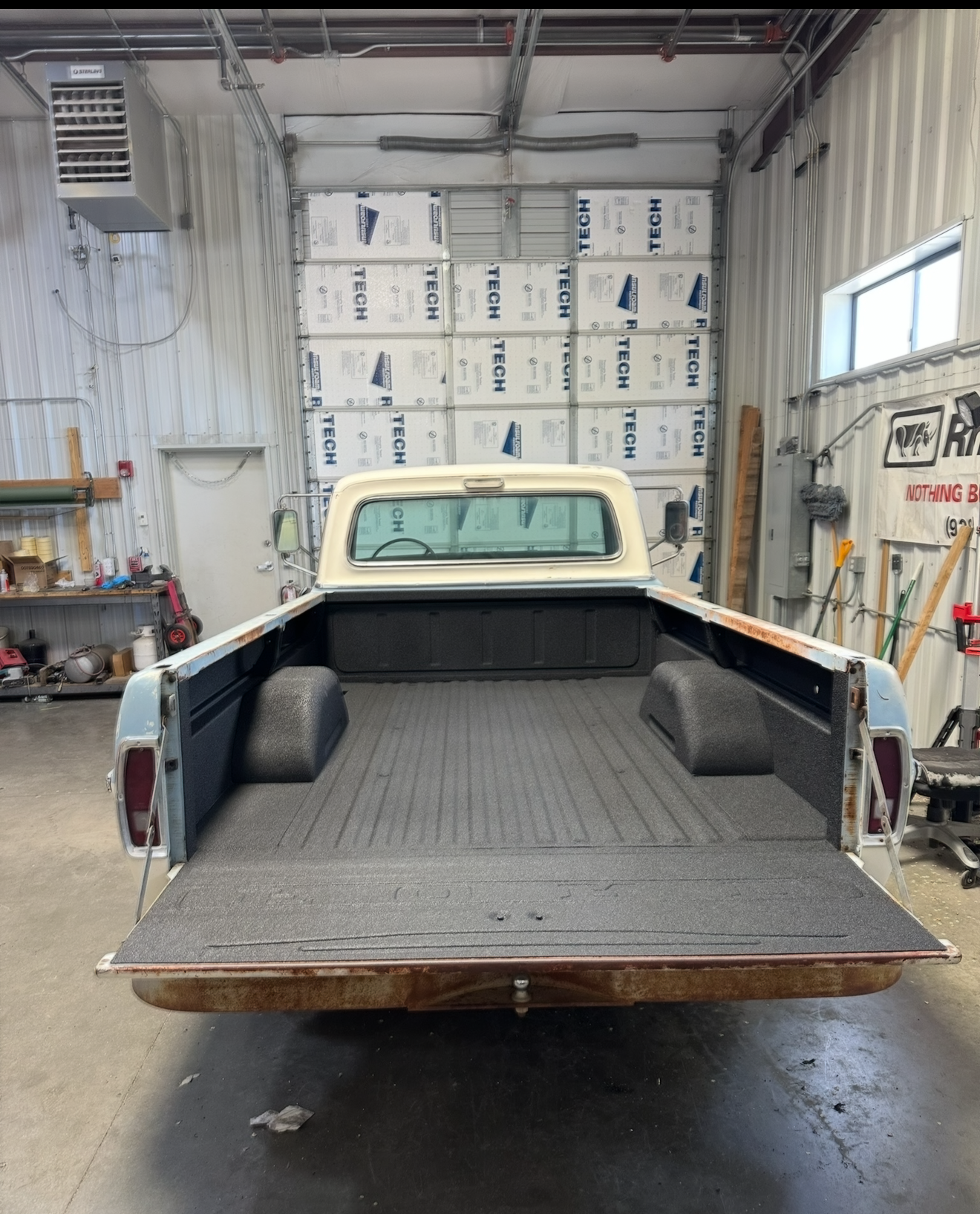 Blue and white vintage pickup truck bed with a textured black liner. Truck is in a workshop.