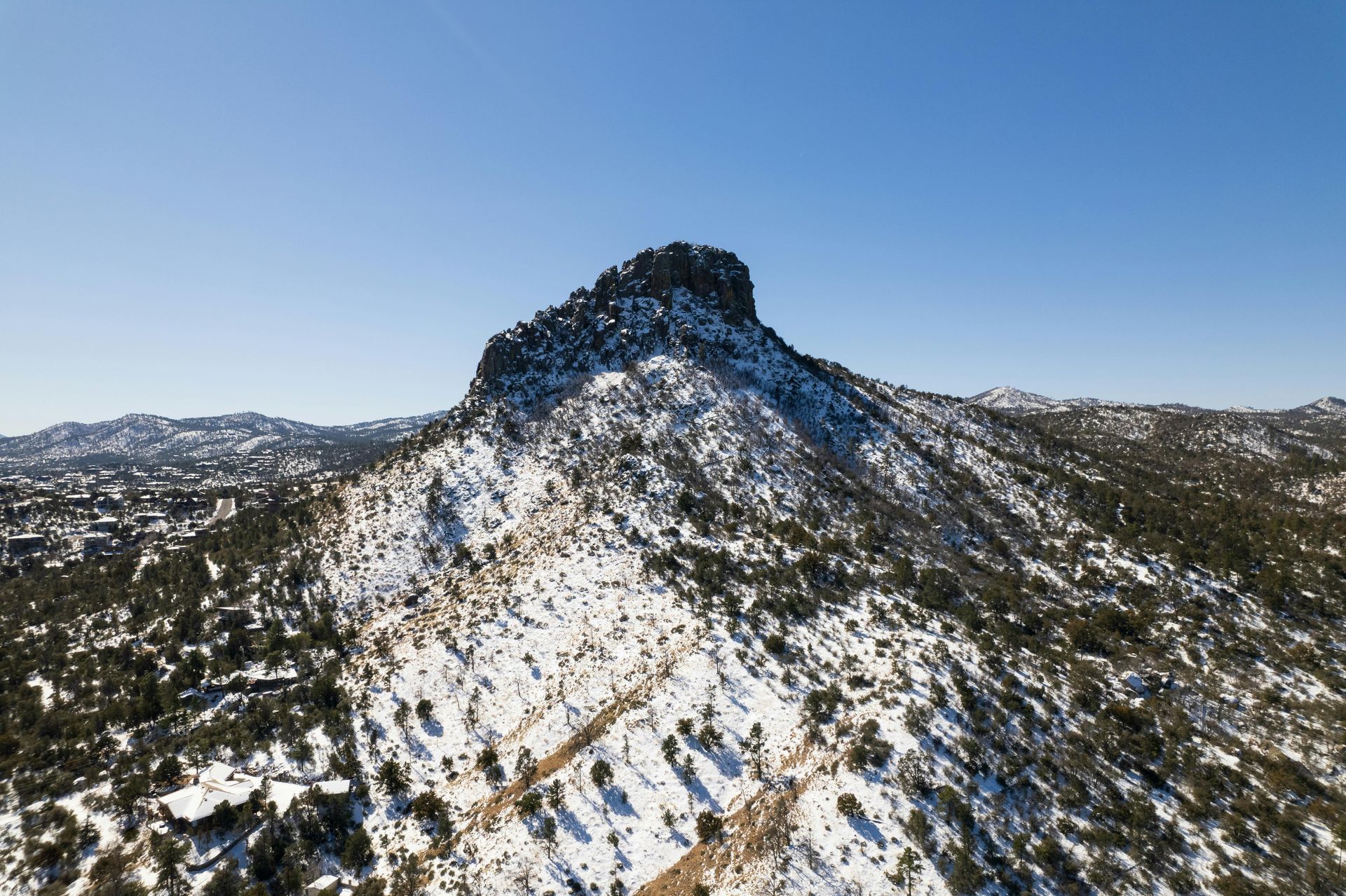 Snow-covered mountain peak against a clear blue sky, with sparse trees and a rocky summit.