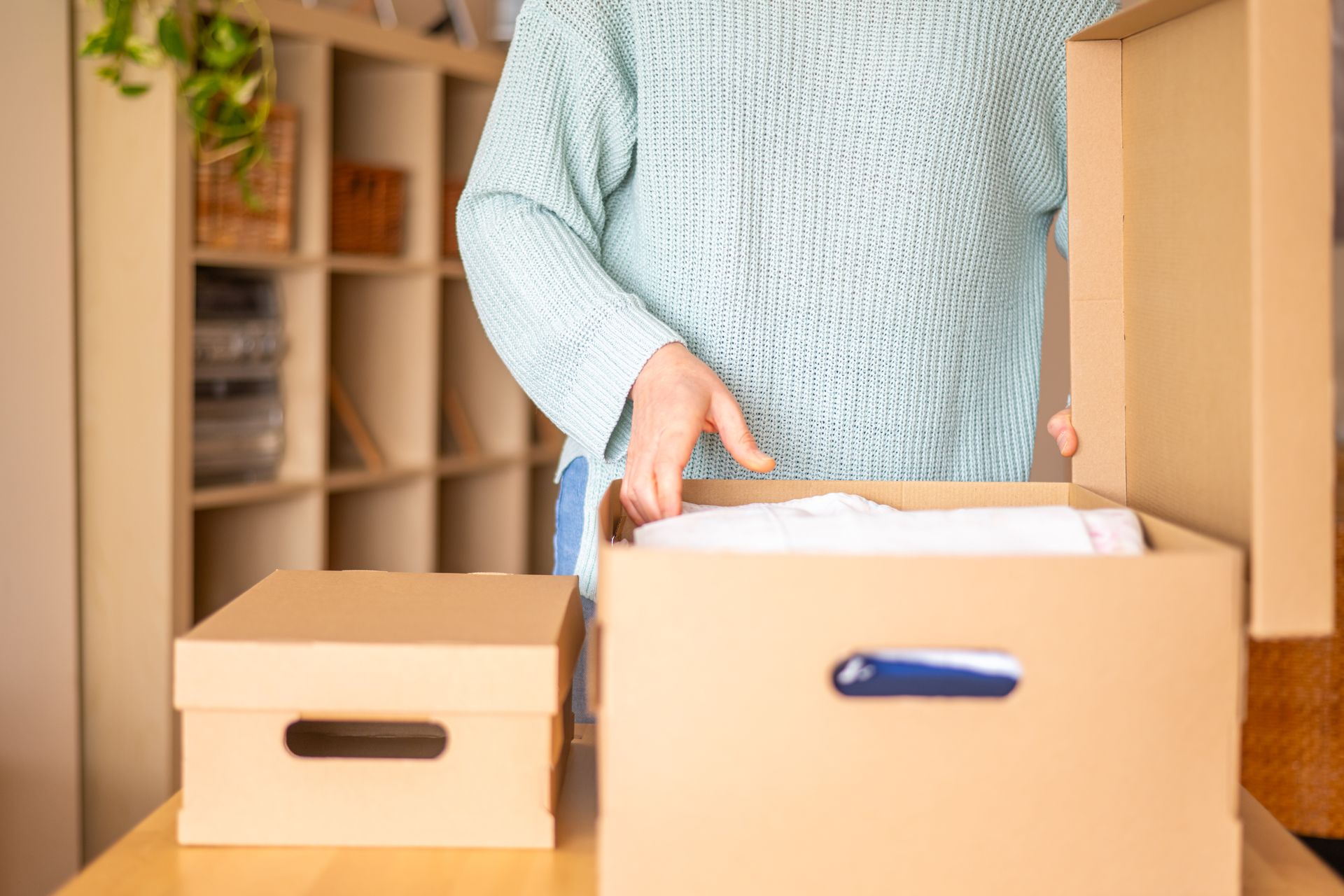 Person packing a cardboard box at a table beside another closed box Person packing a cardboard box at a table beside another closed box