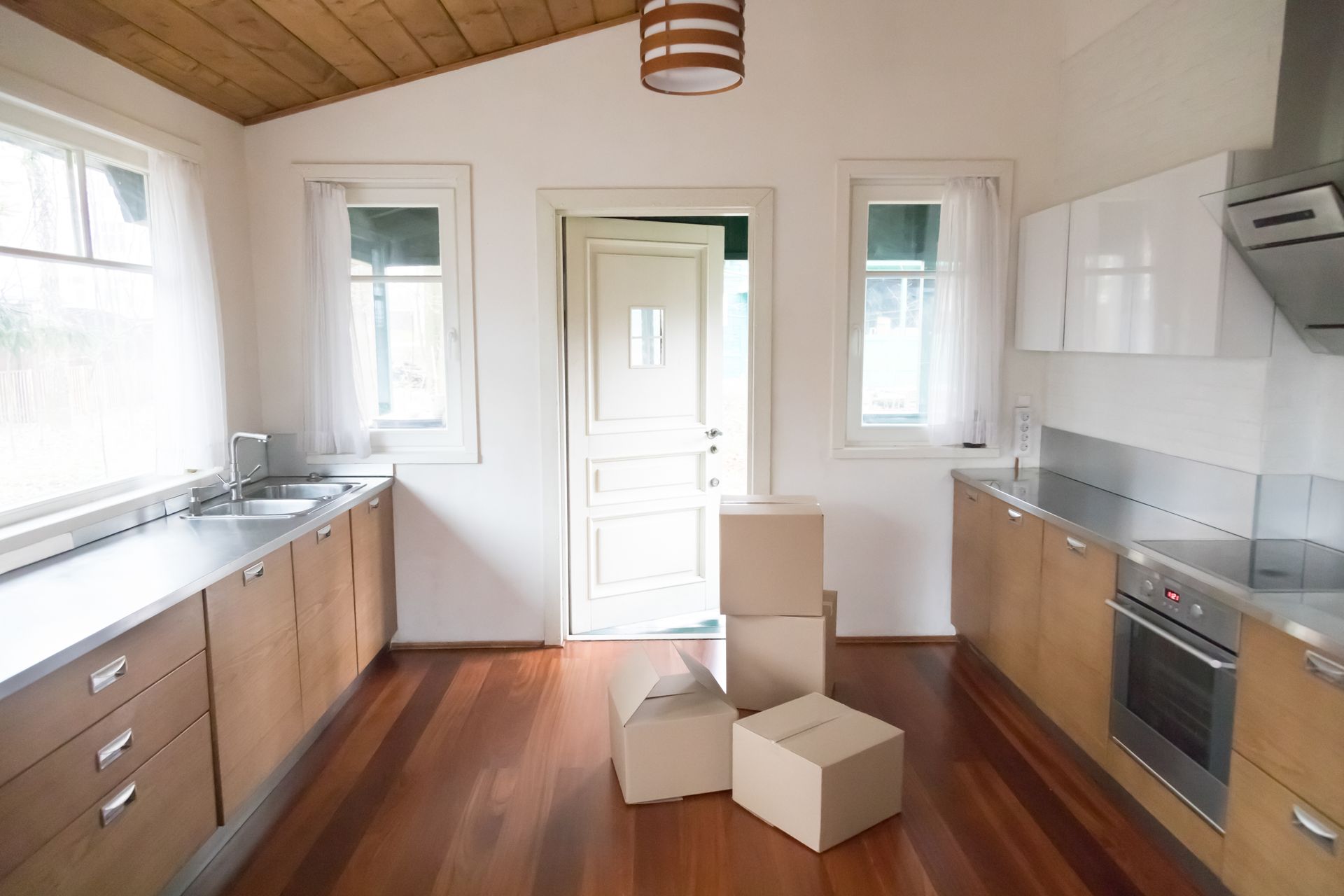 Empty modern kitchen with white cabinets, wood ceiling, and moving boxes on the floor Empty modern kitchen with white cabinets, wood ceiling, and moving boxes on the floor