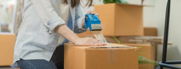 Person taping a cardboard box on a moving truck with packing boxes in the background Person taping a cardboard box on a moving truck with packing boxes in the background