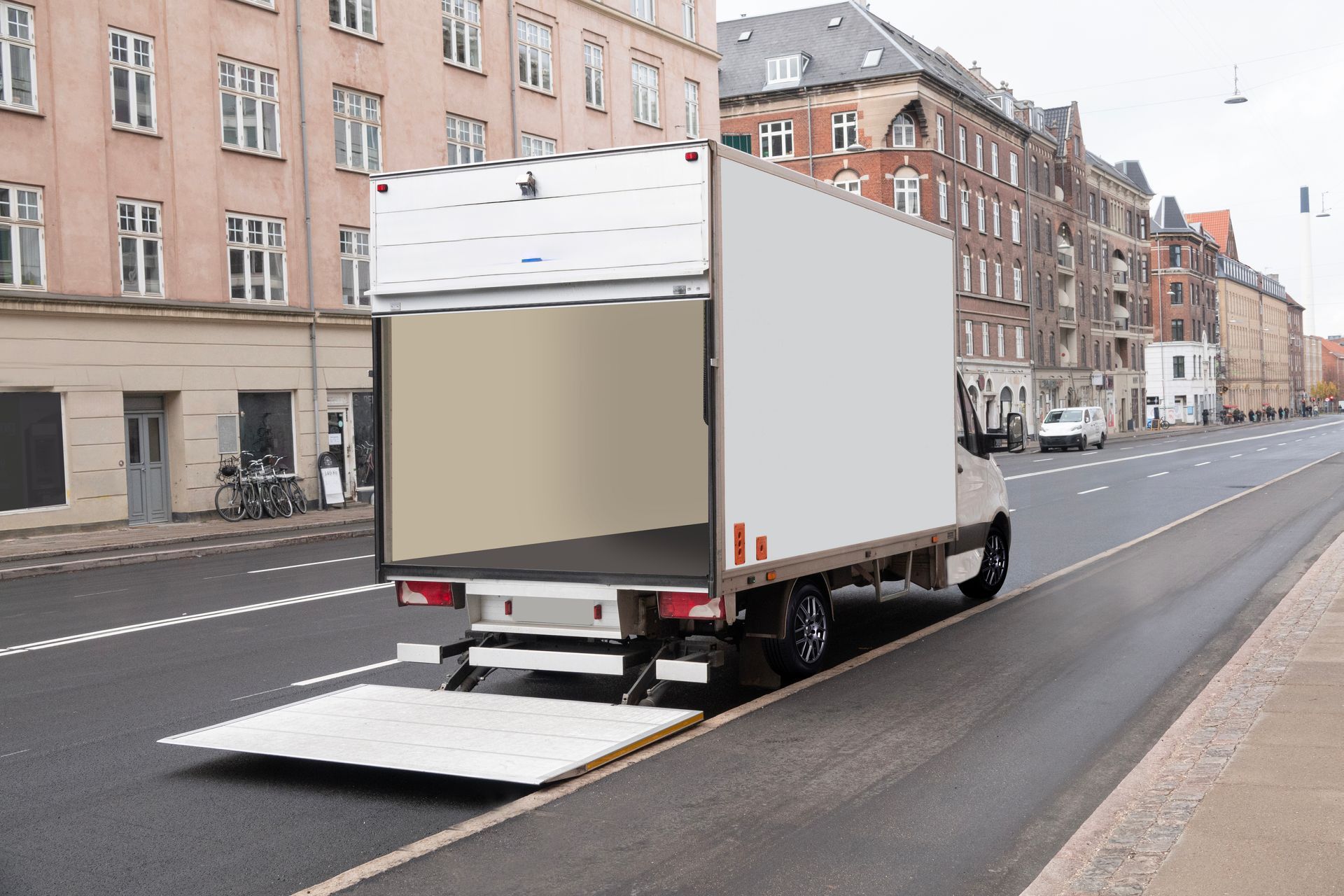 White box truck with open rear ramp parked on a city street lined with buildings White box truck with open rear ramp parked on a city street lined with buildings