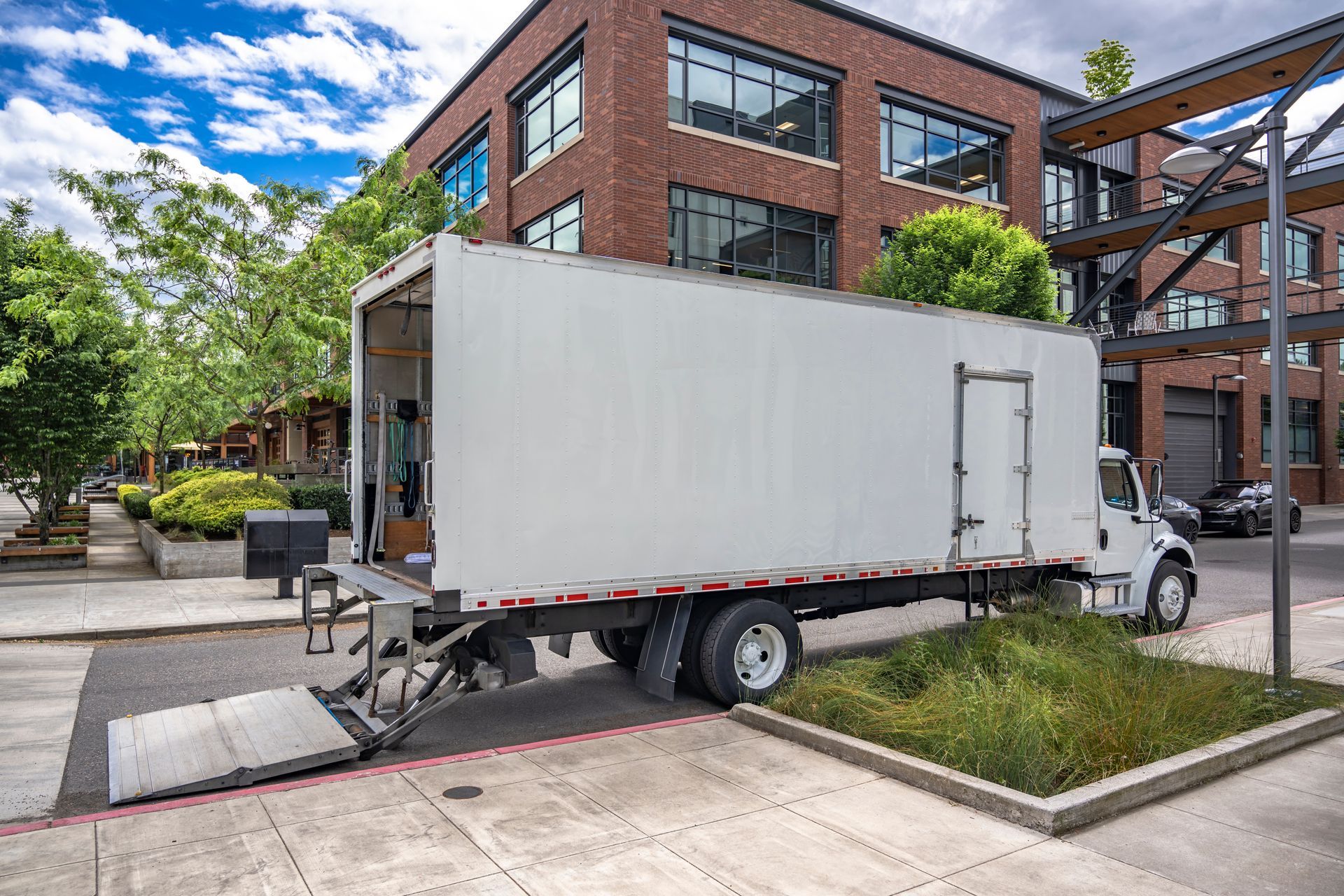 White box truck parked on a city sidewalk with its ramp down beside a brick building. White box truck parked on a city sidewalk with its ramp down beside a brick building.
