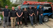 Six workers stand beside a white service van with ladders and tools in a driveway.