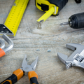 Assorted hand tools on a wooden workbench, including pliers, a wrench, a utility knife, and a tape measure
