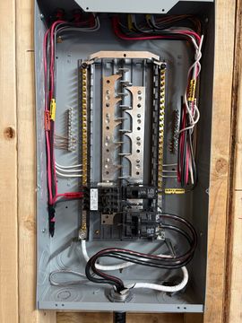 Framed house interior with exposed wiring and an electrical panel in the center wall