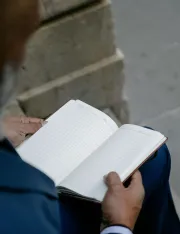 Person holding an open notebook and writing, seated outdoors on stone steps.
