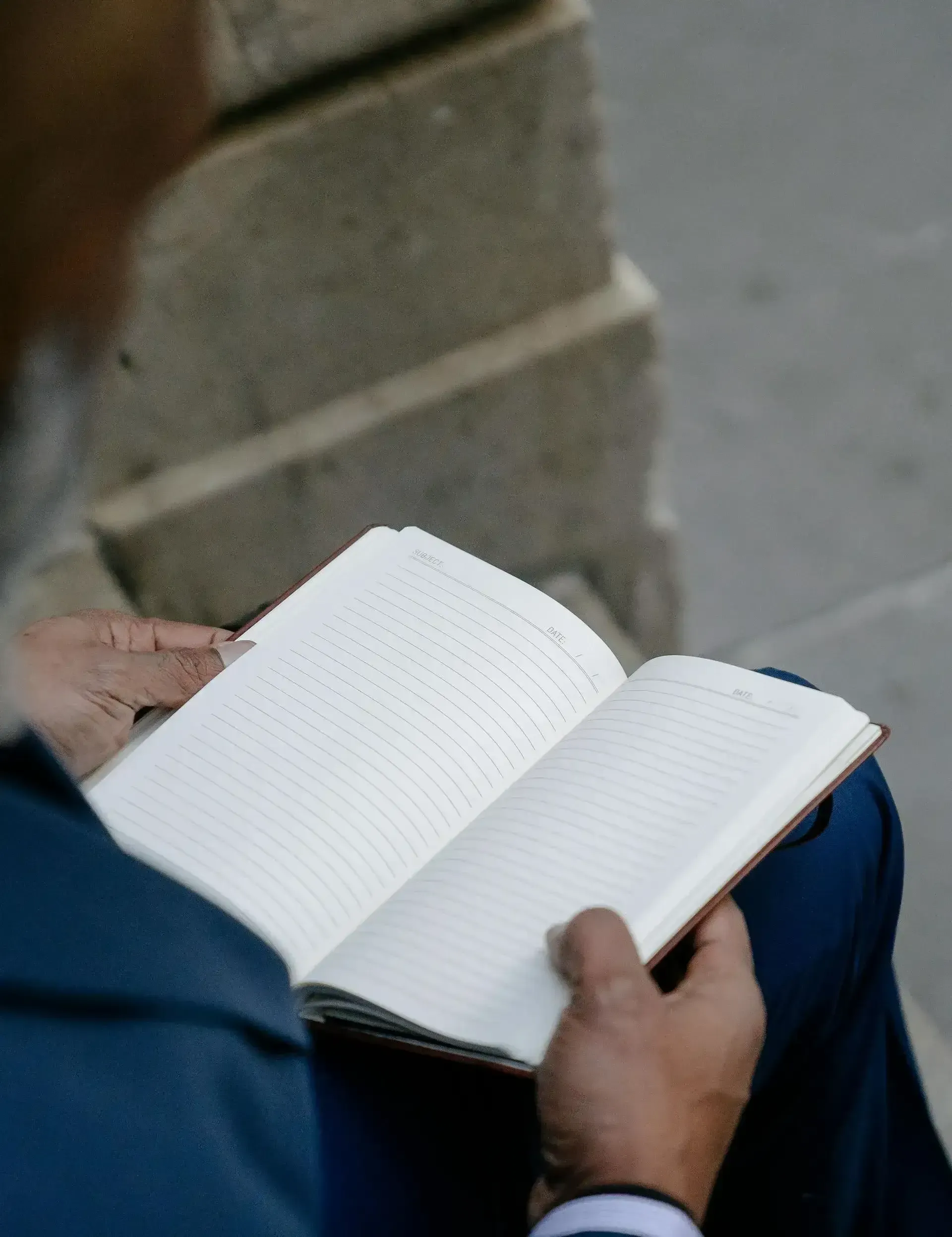 Person holding an open notebook and writing, seated outdoors on stone steps.