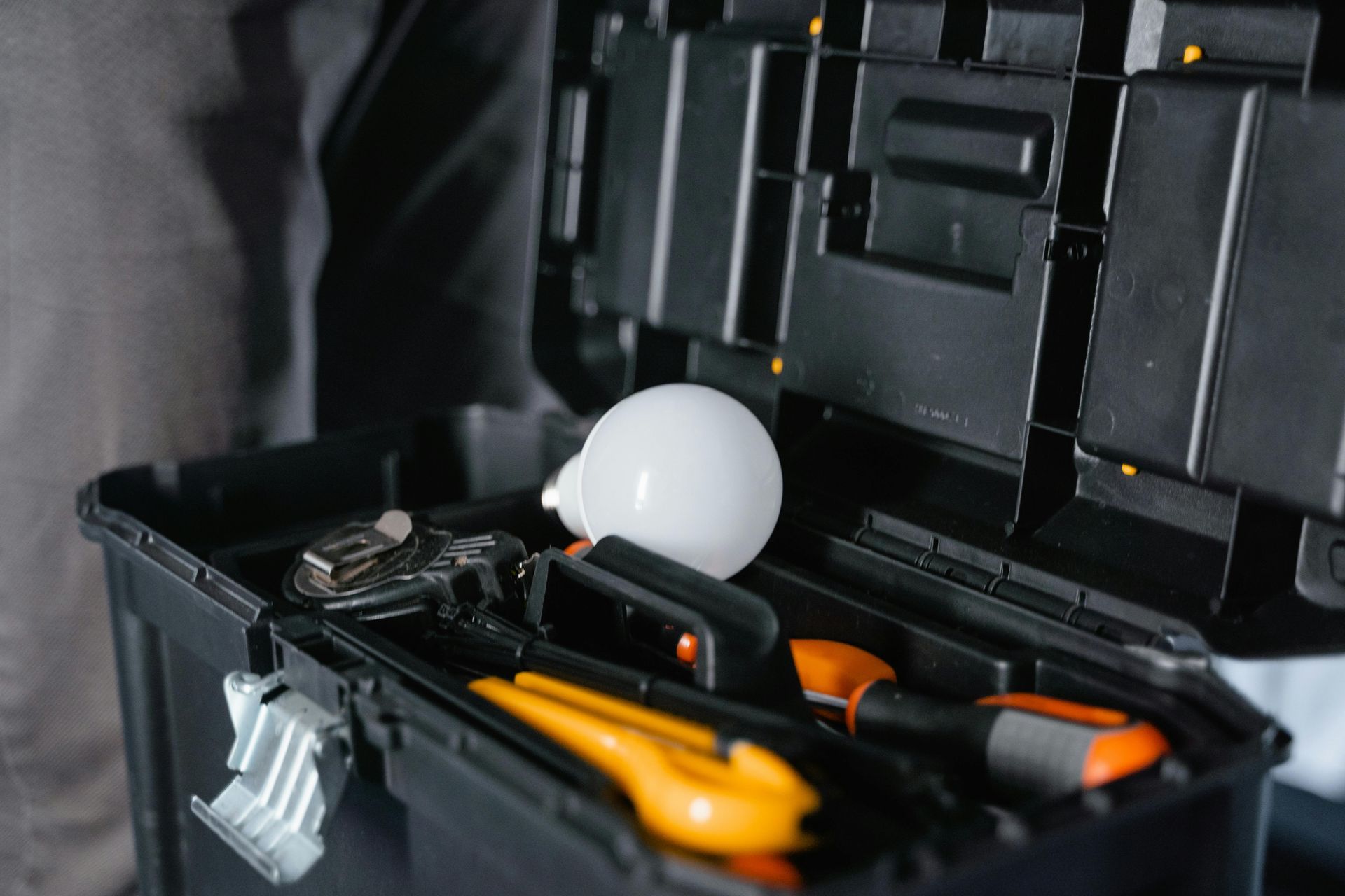 Open toolbox with assorted hand tools and a white bulb inside a black case