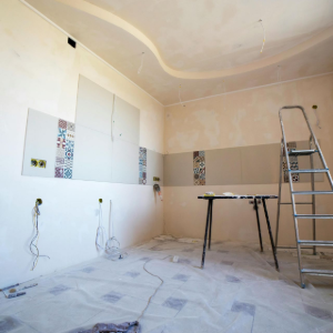 Empty room under renovation with ladder, sawhorses, taped walls, and protective floor covering