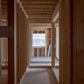 Wood-framed hallway in an unfinished house, with a bright window at the far end.