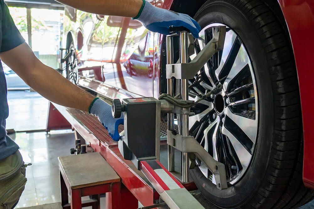 Mechanic aligning a red car's tire with a gauge in a garage, wearing gloves.