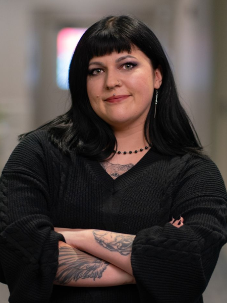 A woman wearing glasses and a pink jacket is standing in front of a tree.