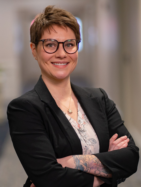 A woman wearing glasses and a black jacket smiles for the camera