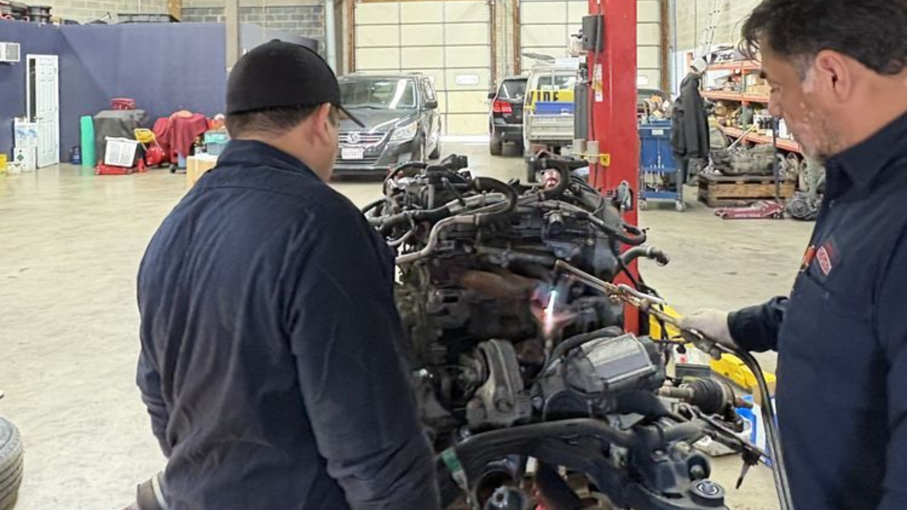 Two mechanics use a welding torch on an engine in a professional auto repair shop.