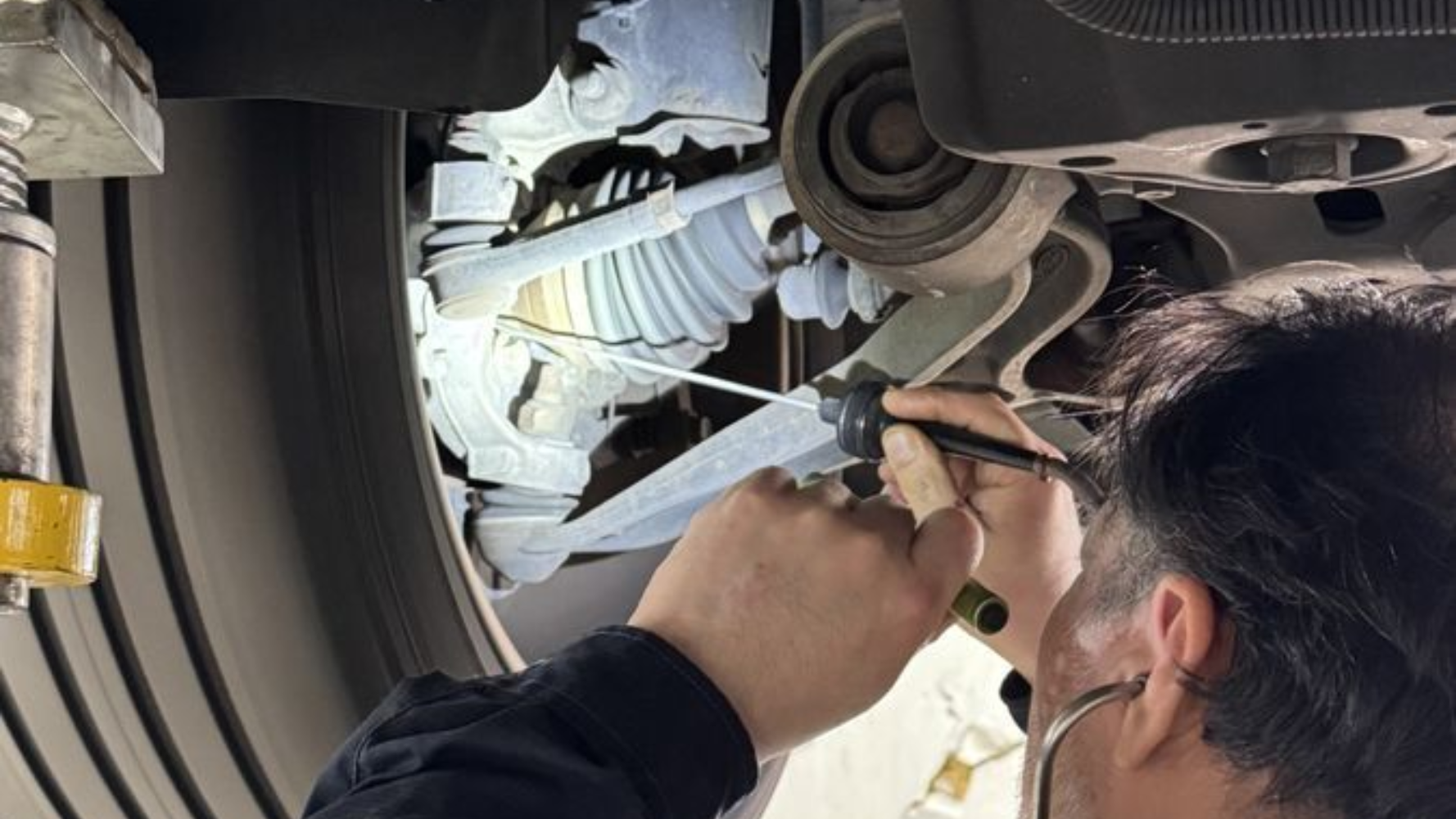 A mechanic inspects a car's front suspension system while the vehicle is raised on a lift.