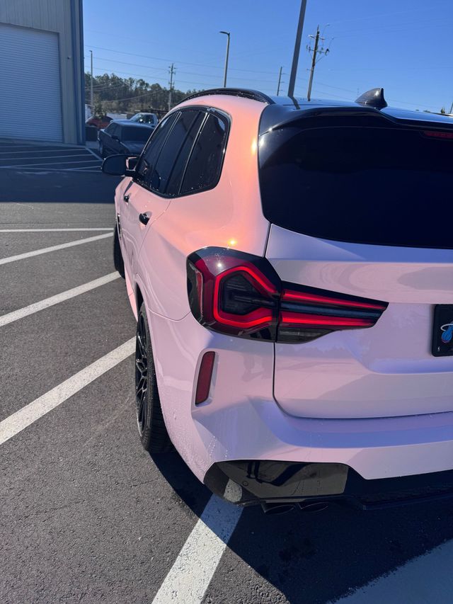 Pink iridescent SUV parked outdoors. Black tinted windows, black rims, and a sunny day.