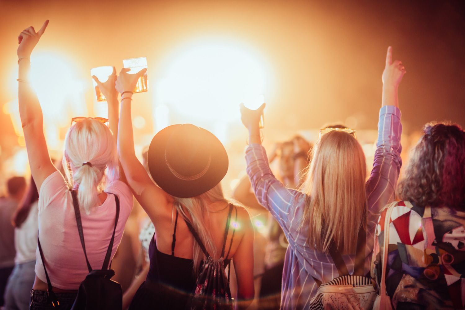 back view of group of female friends at music festival drinking beer and dancing