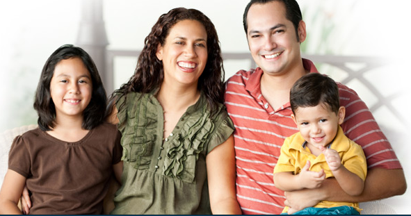 Family of four sitting on a couch, smiling at the camera.