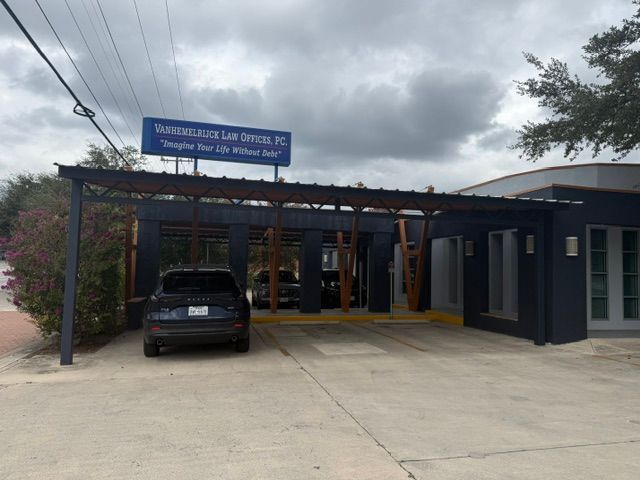 Blue sign above a small building entrance with a black SUV parked under a pergola, under cloudy skies