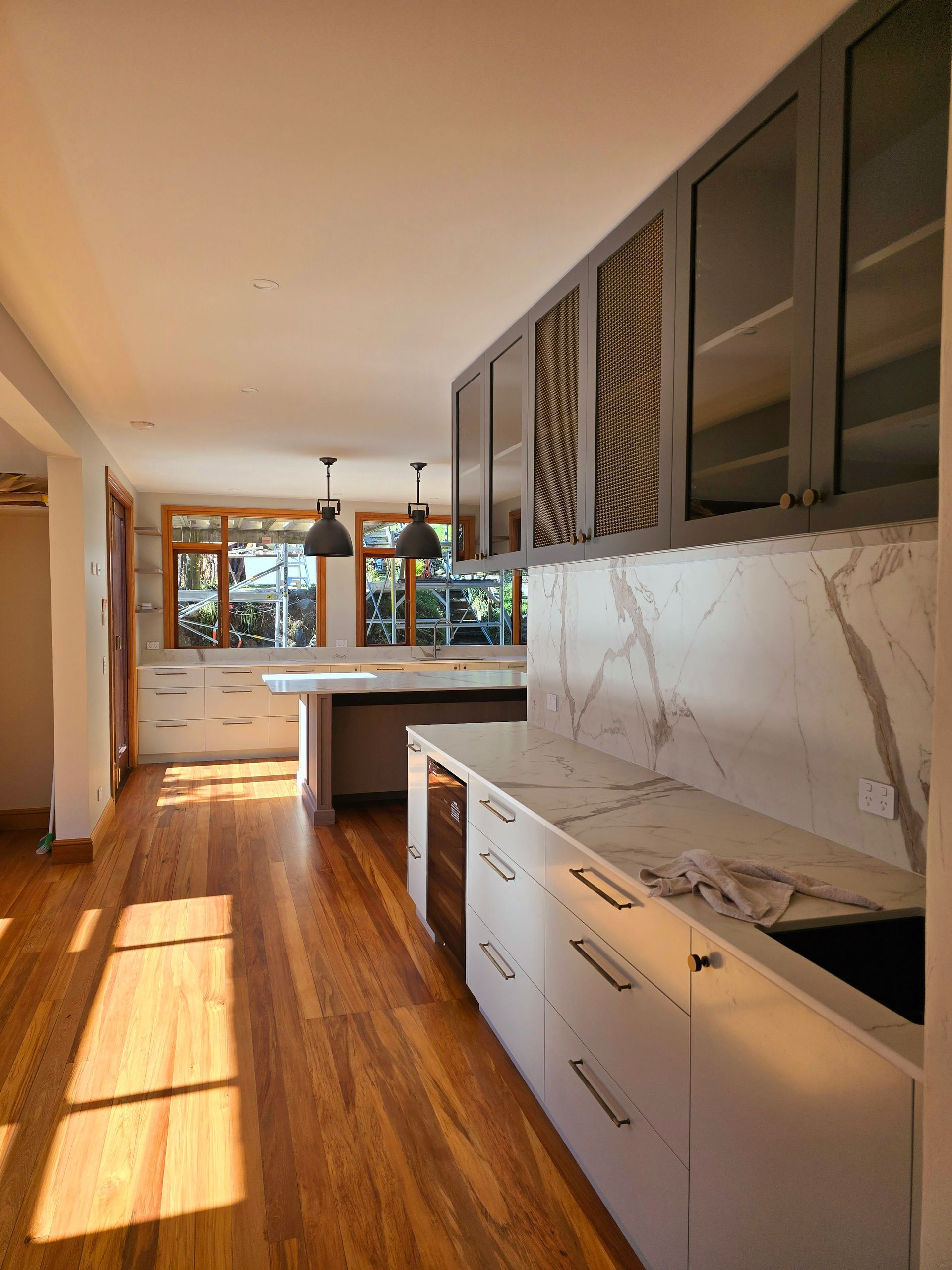 Bright kitchen with wood floors, white cabinets, marble backsplash, and sunlight streaming through large windows.