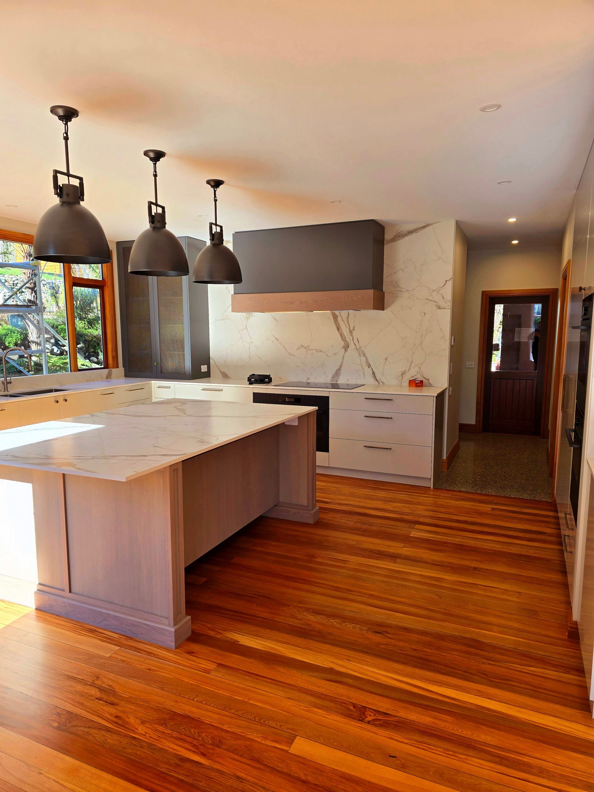 Modern kitchen with wood floors, white island, black pendant lights, and large windowlight.