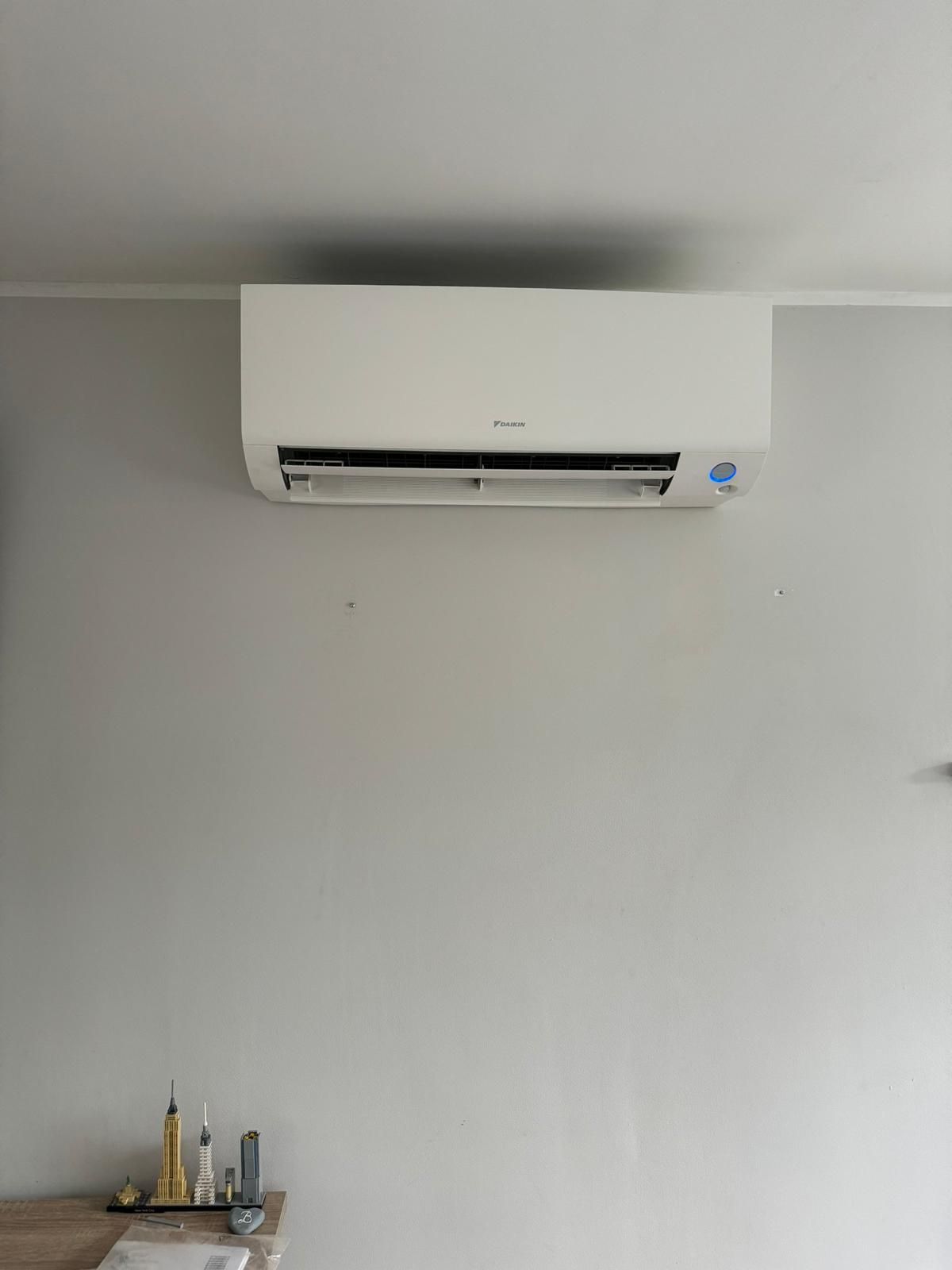 White wall-mounted air conditioner above a small shelf in a plain room.
