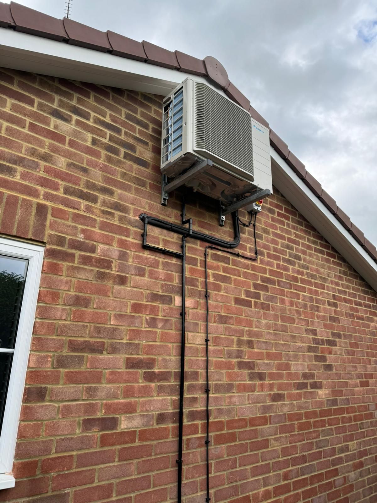 Wall-mounted air conditioning unit on a brick house exterior under a cloudy sky
