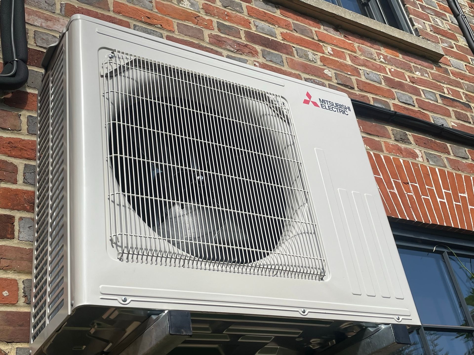 White Mitsubishi electric outdoor AC unit mounted on a brick building wall.