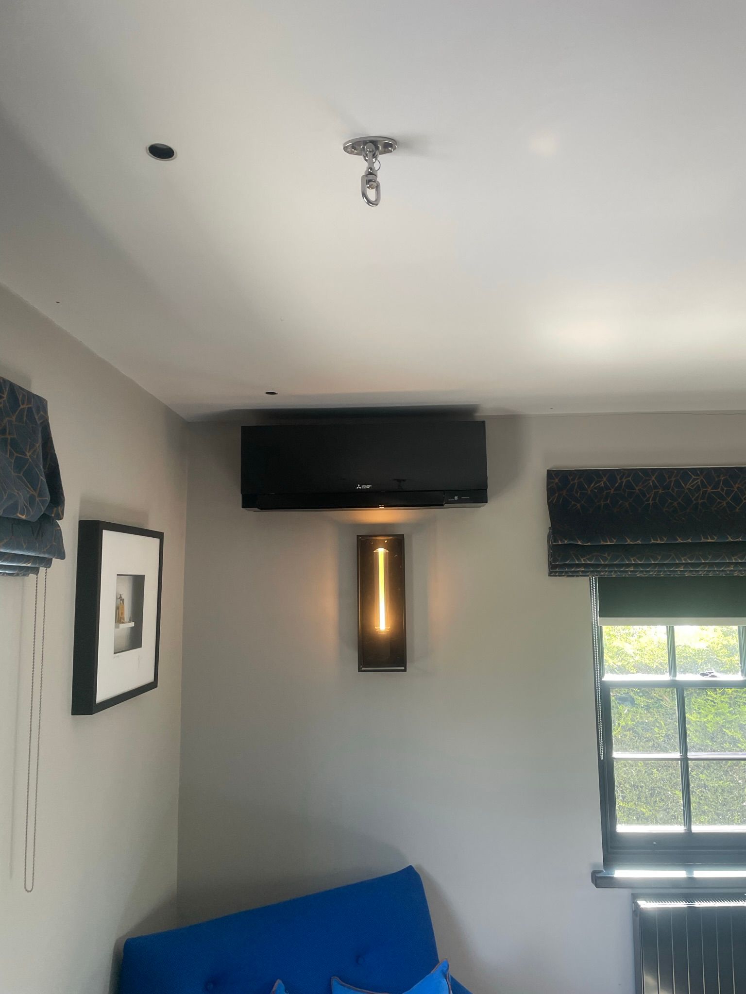 Small room with wall-mounted TV, vertical light fixture, window, and blue couch against white walls.