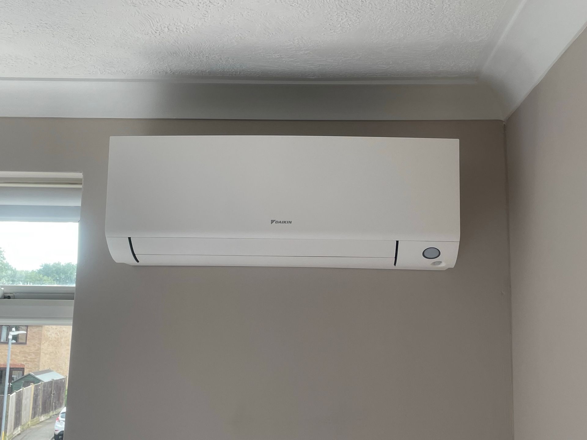 White Daikin wall-mounted air conditioner above a window in a bedroom.