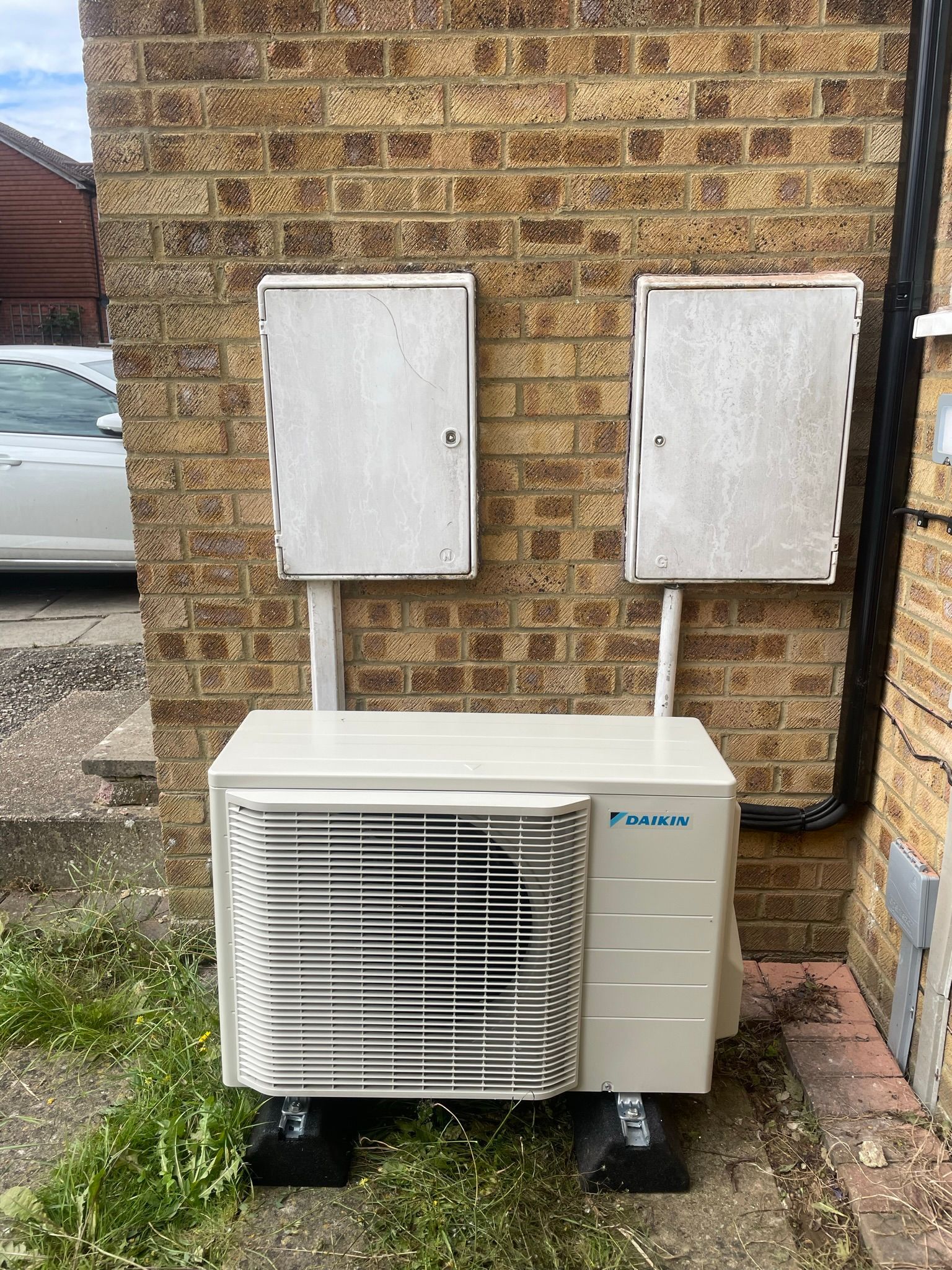 Outdoor HVAC unit beneath two white electrical boxes against a brick wall
