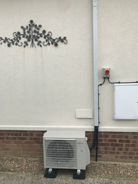 Exterior wall with mounted utility meter, conduit, air conditioning unit, and decorative metal wall art.