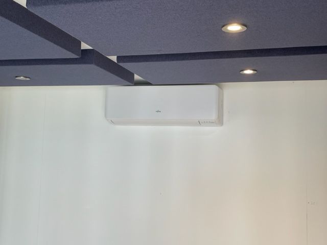 White wall with a mounted air conditioner beneath a dark ceiling with recessed lights