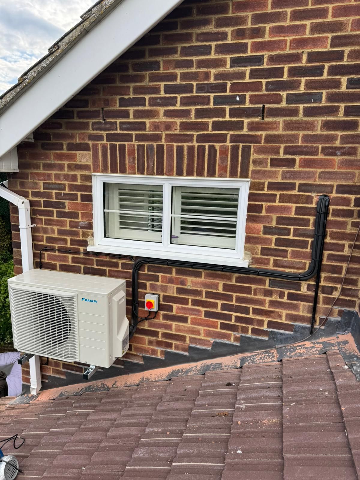Brick house wall with a white window, wall-mounted AC unit, and roofline in view