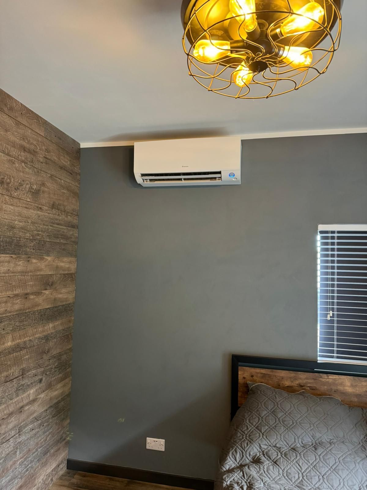 Small bedroom with gray walls, wood accent wall, wall AC, window blinds, bed, and gold ceiling light fixture