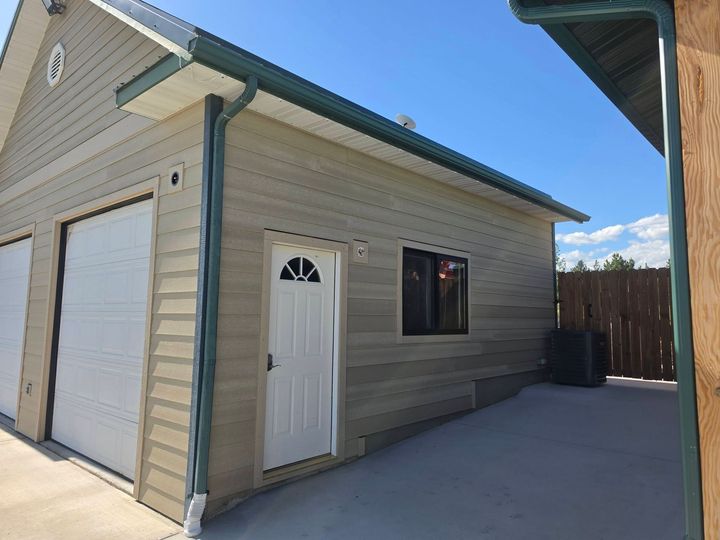 Detached beige garage with white door, side entry, and concrete driveway under a blue sky
