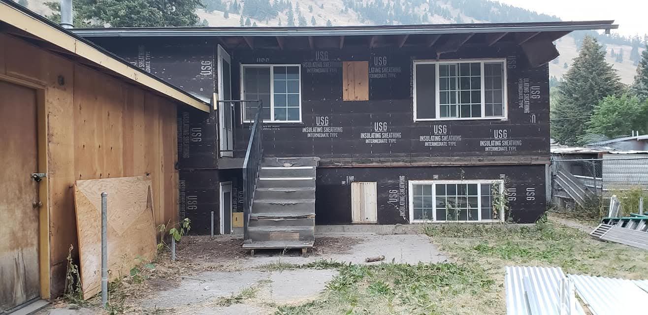 Old dark house with front stairs beside a wooden garage and a gravel yard.