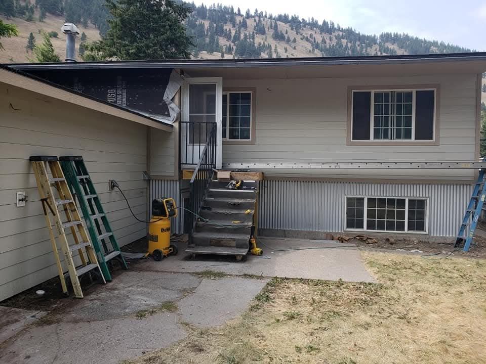 Side view of a house with a carport, ladder, yellow mower, and stairs leading to a back entrance.