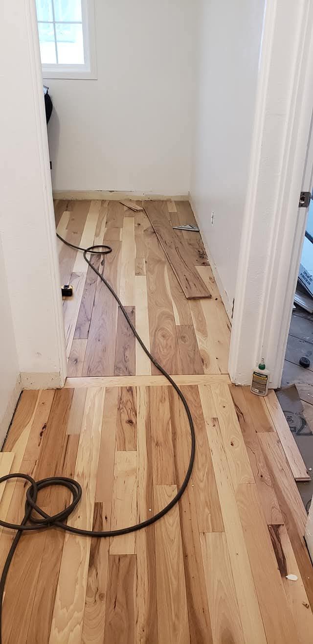 Narrow hallway with stripped wood flooring, tools, and debris during renovation