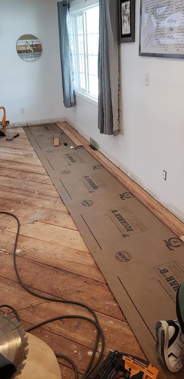 Long hallway with floor repair underway, brown underlayment rolled out on wooden floor, cables visible.