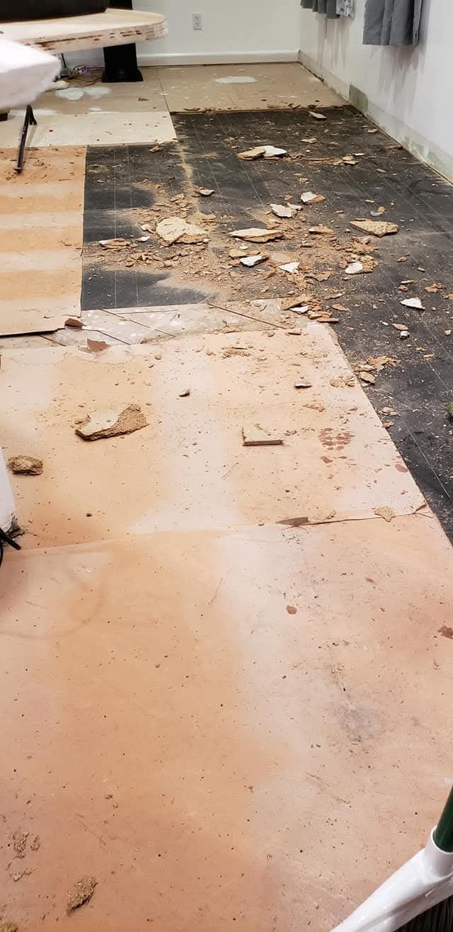 Damaged carpet with exposed floor and debris along a wall in a room