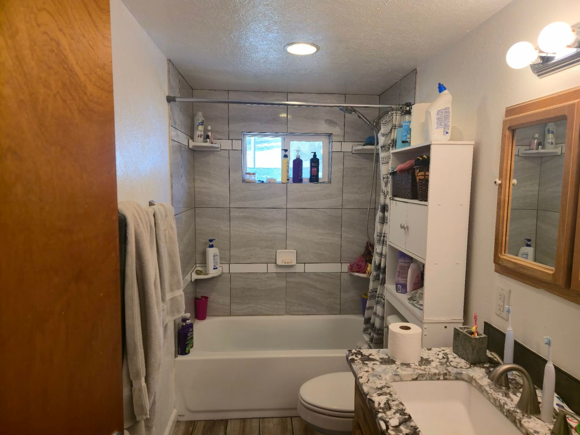 Small bathroom with a tiled shower/bathtub, toilet, sink, and mirror cabinet.