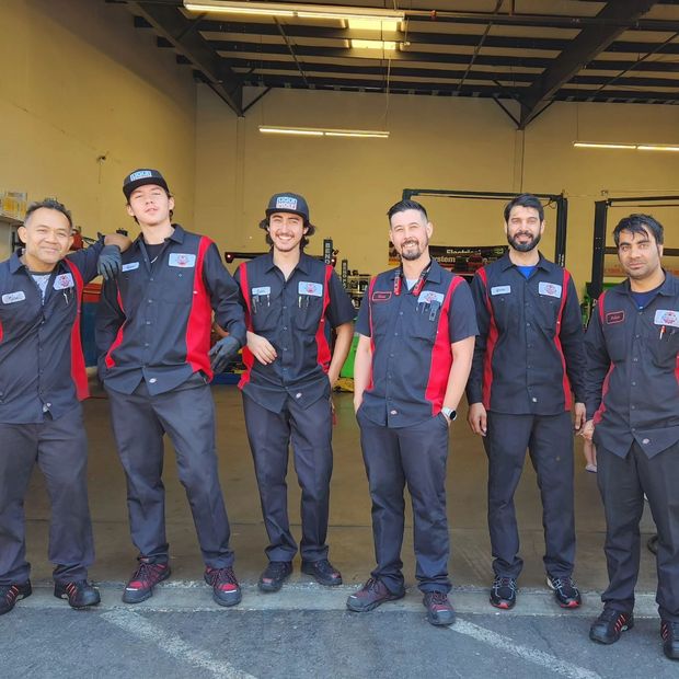 Seven auto mechanics in matching black and red uniforms pose together in a garage | Freebird Automotive
