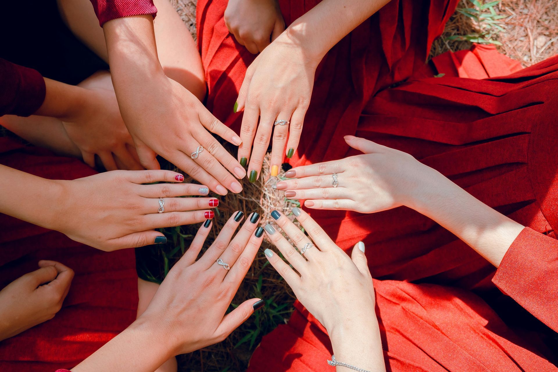 Hands of several people, wearing rings and painted nails, touching in a circle. Red fabric backdrop.