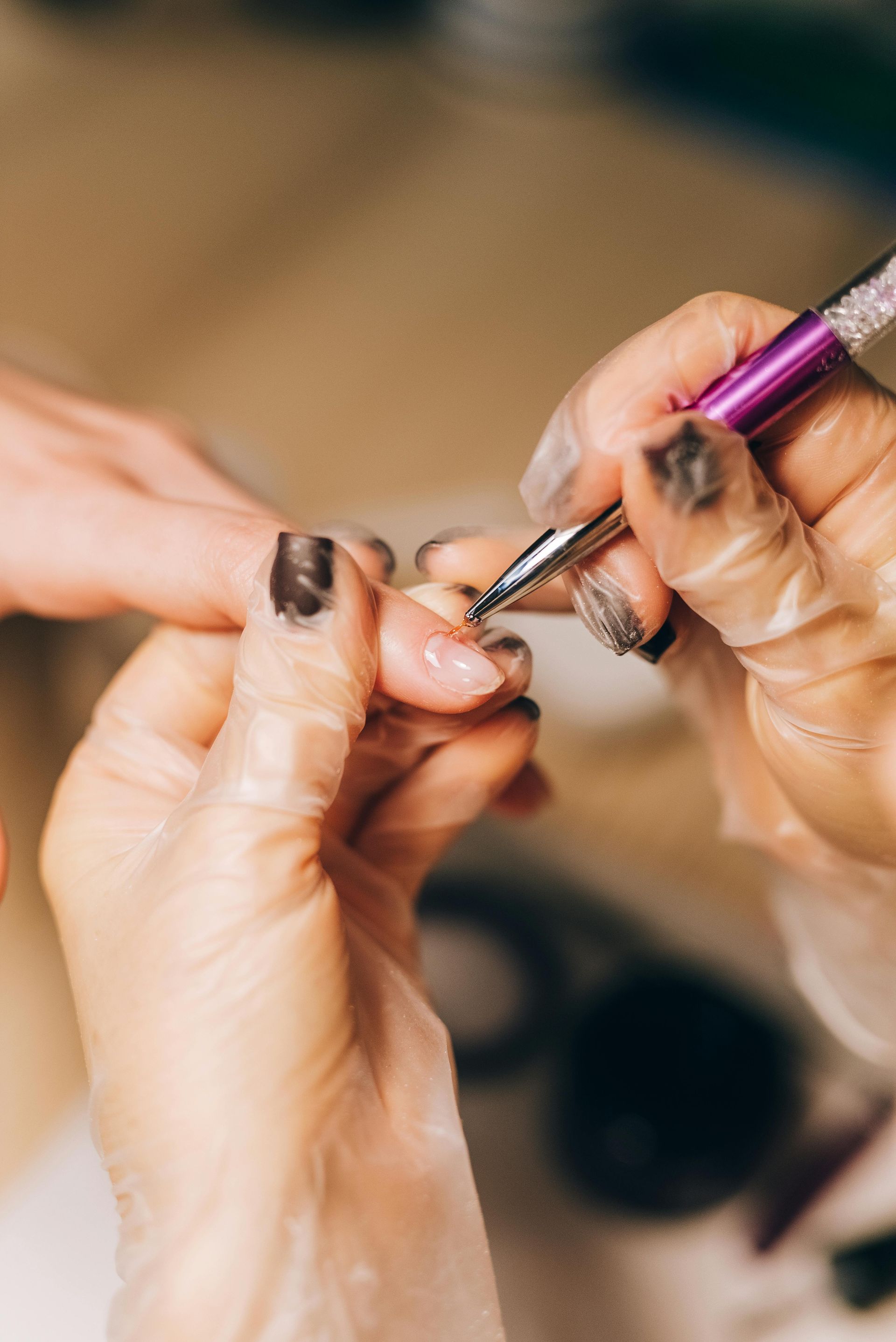 Manicurist's gloved hands applying nail art to a client's fingernail, focus on the tool and the nail.